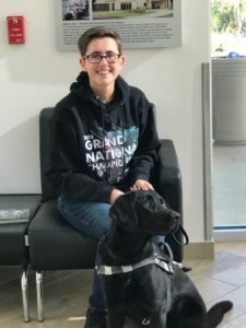 Teen transition client sits with the guide dog and smiles looking at the camera.