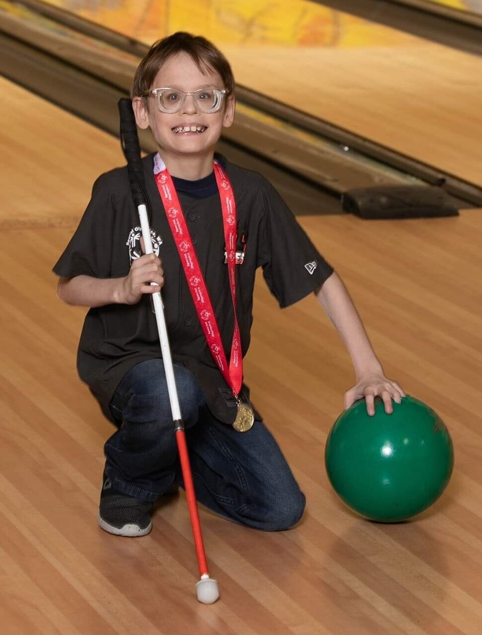 Luke holding his cane and a bowling ball, posing for the camera at the bowling alley